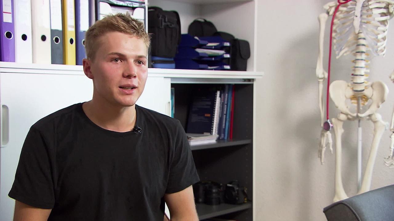 © ORF / Matthias Witzemann Am Bild sitzt ein junger blonder Mann im schwarzen T-shirt vor einem Kasten mit Aktenordnern und Büchern. neben ihm steht ein Modell eines Skelettes. Er möchte Medizin studieren.