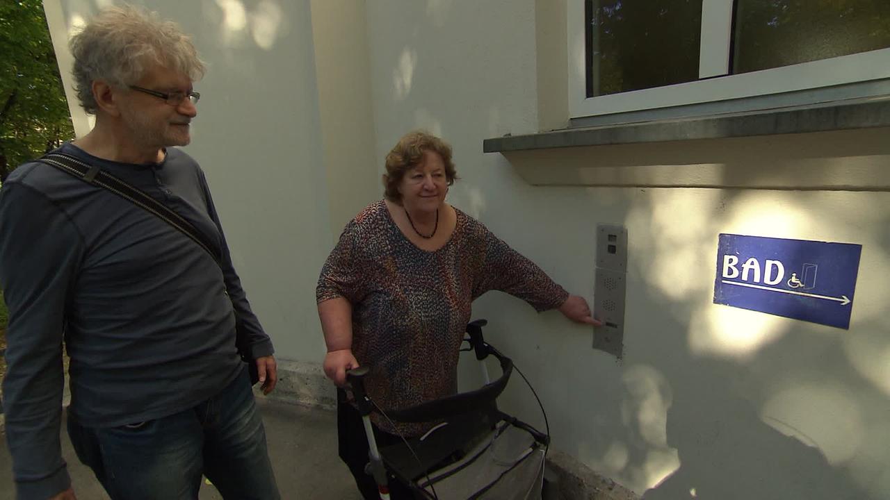 Die 65-jährige Frau Dr. H. steht mit Rollator beim Seiteneingang zum Amalienbad. Sie läutet, damit sie jemand einlässt. Neben ihr steht ihr Mann, der sie begleitet.