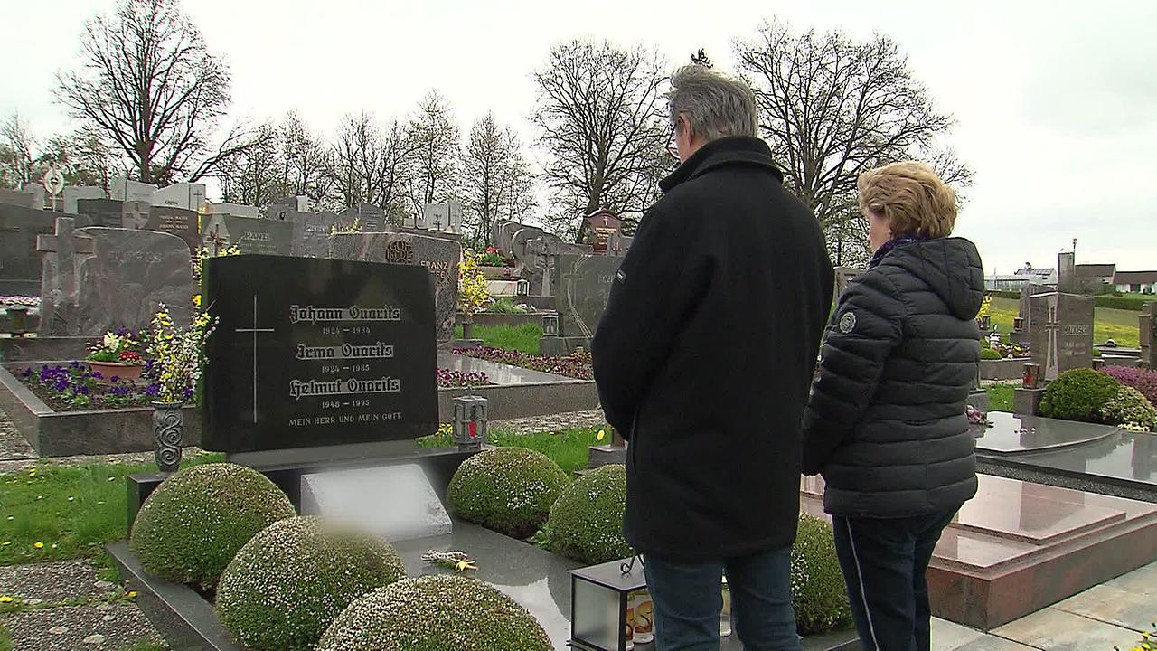 Das Ehepaar W. steht am Friedhof und betrachtet andächtig ihr Familiengrab.
