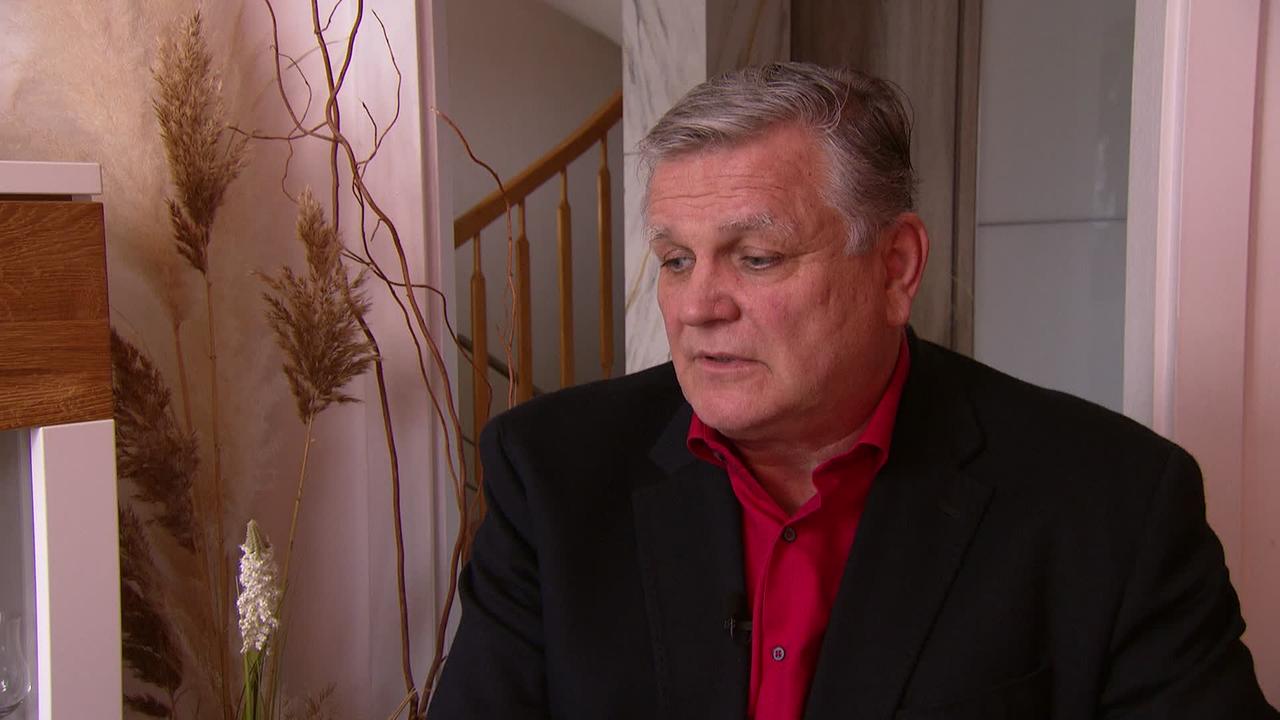 © ORF / Gustl Gschwantner Am Bild ist der 63jährige Herr G. in seinem zu Hause zu sehen. Er trägt einen dunklen Blazer und ein rotes Hemd.