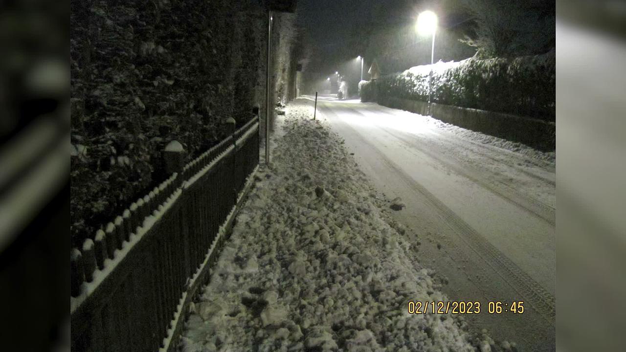 Man sieht ein Foto vom 02.12.23 um 06:45 Uhr. Es ist eine Straße im Winter zu sehen mit etwas Schnee auf der Fahrbahn und jede Menge zusammen geschobener Schnee am Gehsteig, den der Schneepflug dort hingeschoben hat.