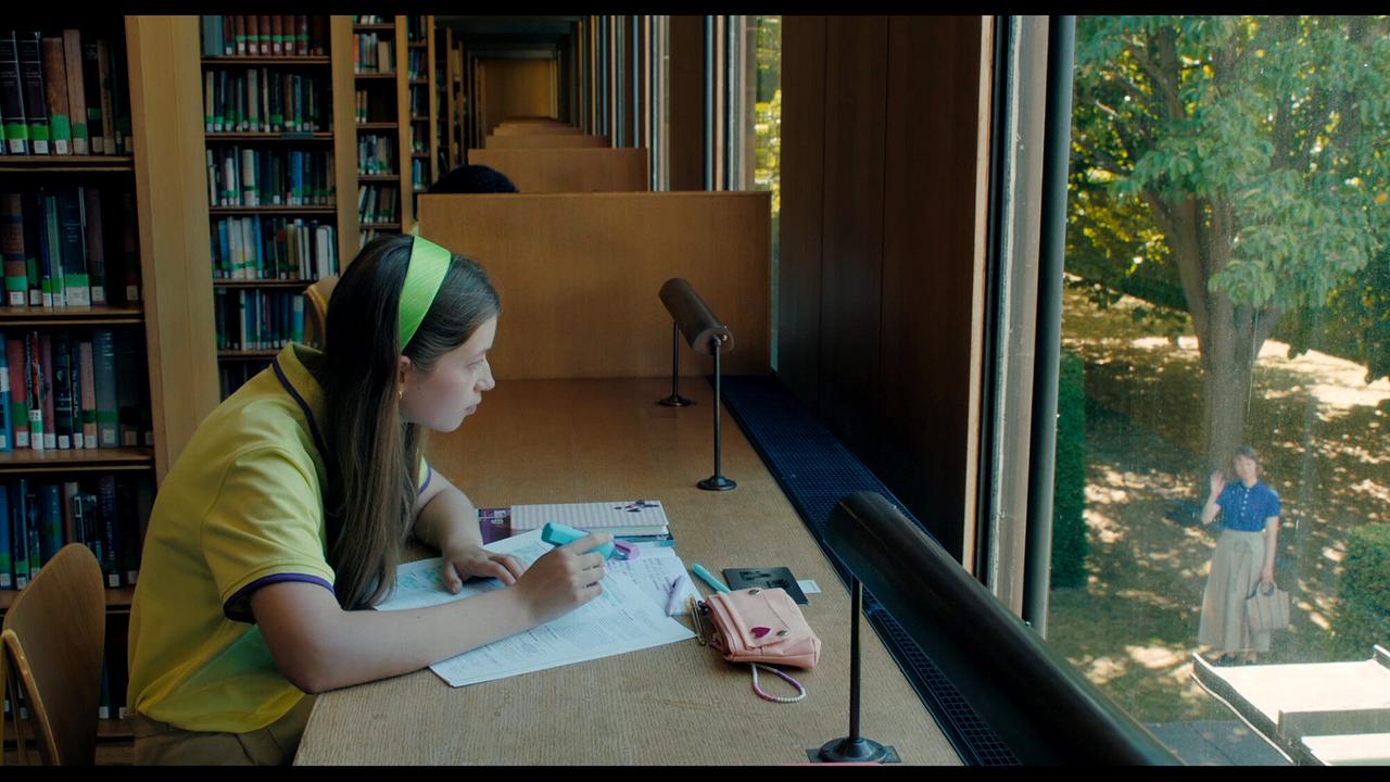 In einer Bibliothek lernt Elsa am Fensterplatz, draußen steht MS Novak im Grünen und winkt ihr zu.