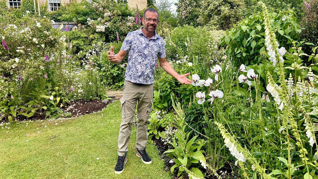 Karl Ploberger im Garten neben weißen Blumen
