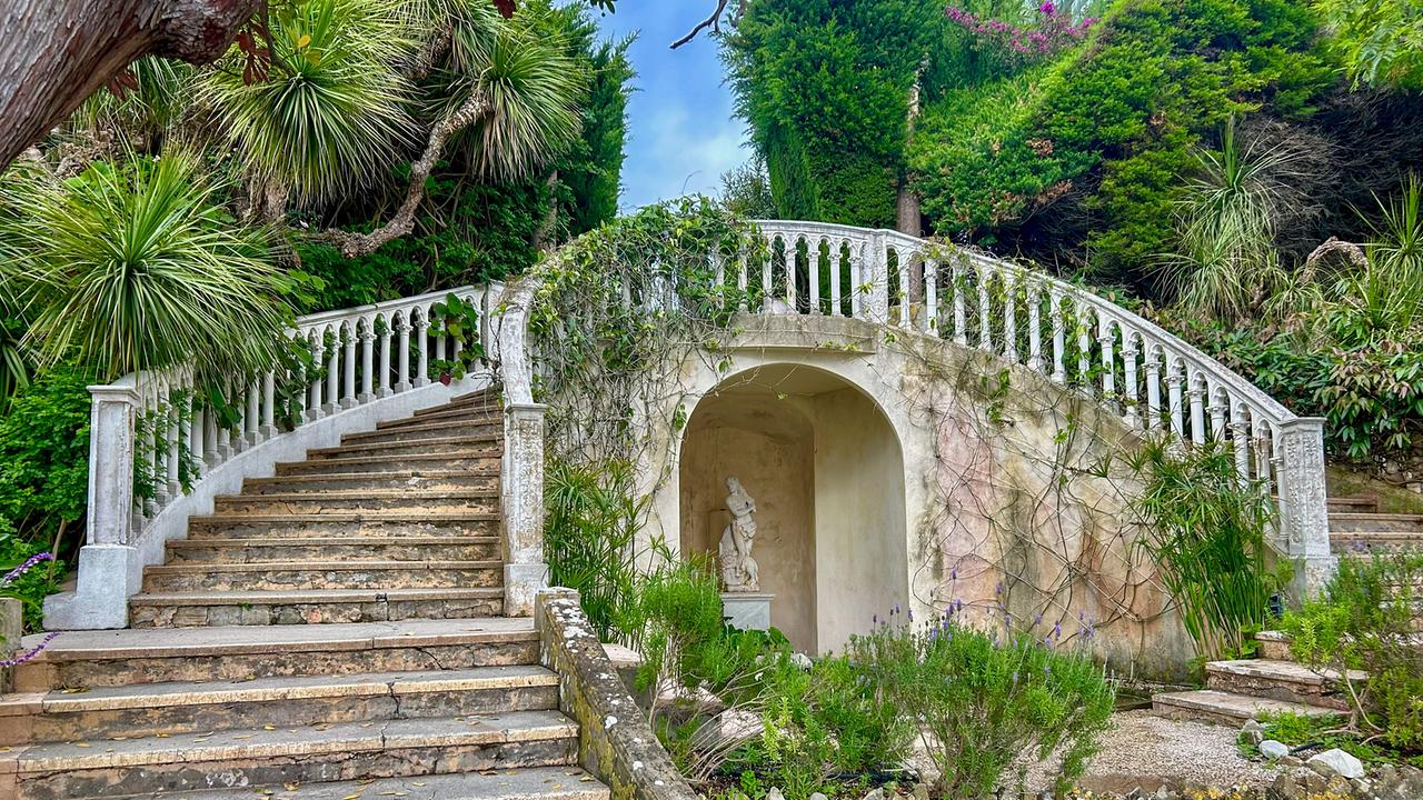 © ORF/Ralph Huber-Blechinger Geschwungene Steintreppe mit Balustrade und einer Nische mit Statue, umgeben von üppigem Grün in den Themengärten der Villa Ephrussi de Rothschild