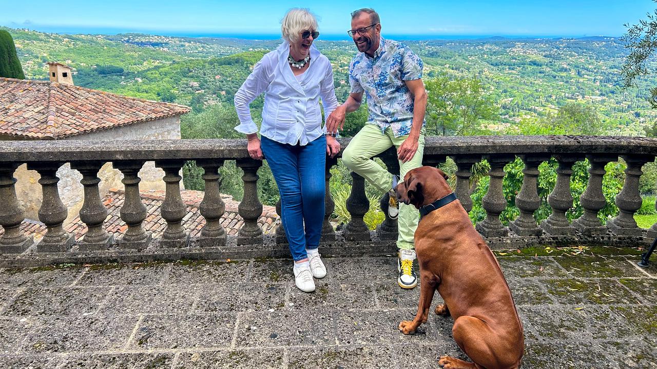 © ORF/Ralph Huber-Blechinger Zwei Personen lehnen an einer steinernen Balustrade mit Blick auf eine grüne Landschaft und das Meer, ein großer brauner Hund sitzt auf dem Boden davor.