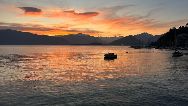 Sonnenuntergang am Lago Maggiore,  während ein einzelnes Boot vor einer dunklen Bergsilhouette treibt.