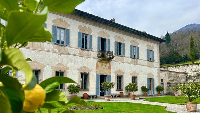 Ansicht der Villa Della Porta Bozzolo mit hellen Fensterläden, gepflegtem Garten und Zitronenbaum im Vordergrund vor sanfter Hügellandschaft.