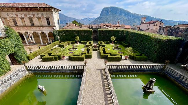 Villa Cicogna Mozzoni mit symmetrischen Renaissancegarten mit geschnittenen Hecken, Wasserbecken und historischen Gebäuden vor einer hügeligen Landschaft.