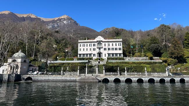 Blick vom Comer See auf die  Villa Carlotta in Tremezzo, terrassenförmig angelegt vor bewaldeten Bergen und spiegelndem Wasser unter tiefblauem Himmel.