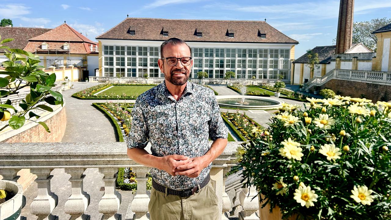 © ORF/Ralph Huber-Blechinger Karl Ploberger steht auf einer Terrasse von Schloss Hof vor einem barocken Garten mit Blumenbeeten und Springbrunnen.