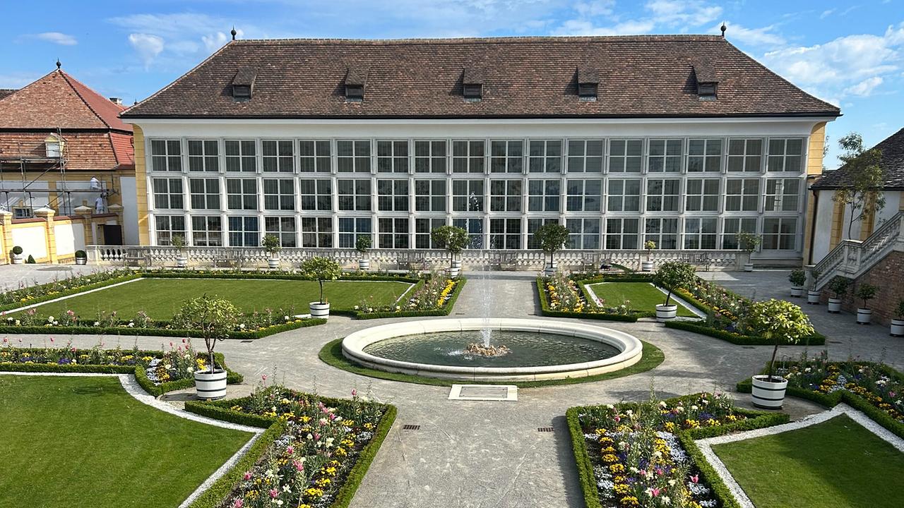 © ORF/Ralph Huber-Blechinger Barockes Schlossgebäude von Schloss Hof mit symmetrisch angelegtem Blumengarten, Springbrunnen und Kieswegen.