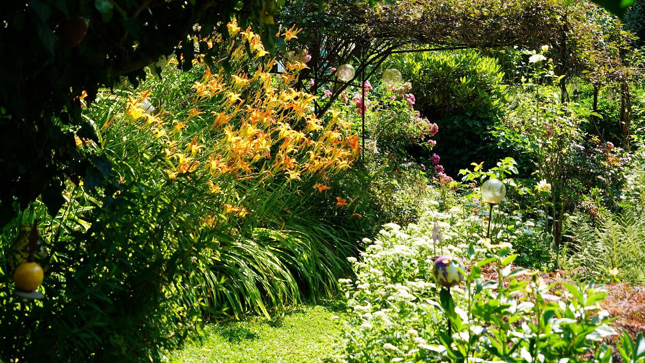 © Leopold Mayrhofer/Natur im Garten Üppiger Terrassengarten mit blühenden Stauden, einem schattigen Laubengang und vielfältiger Bepflanzung.