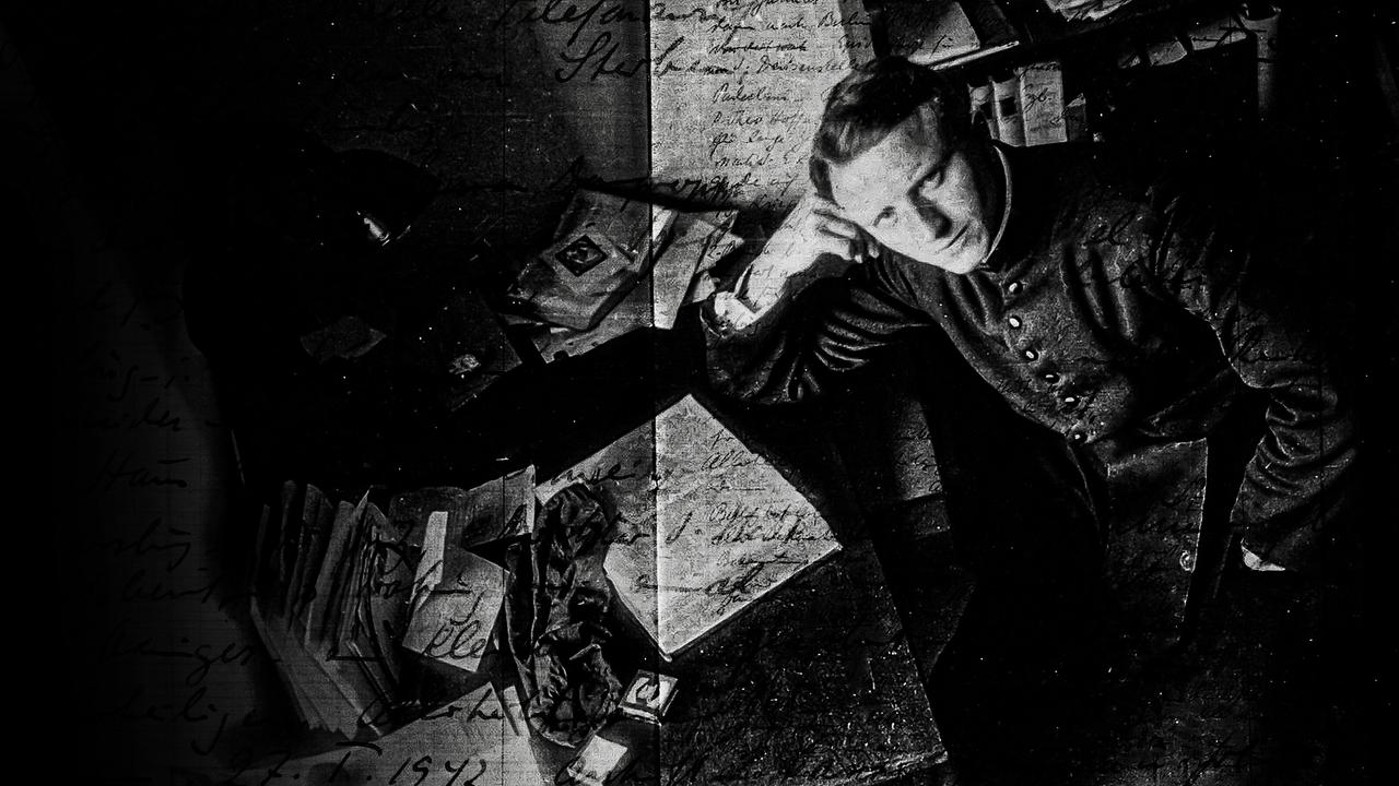 Der deutsche katholische Priester Franz Stock sitzt an einem Schreibtisch voller Dokumente und Briefe und stützt nachdenklich den Kopf auf die Hand.