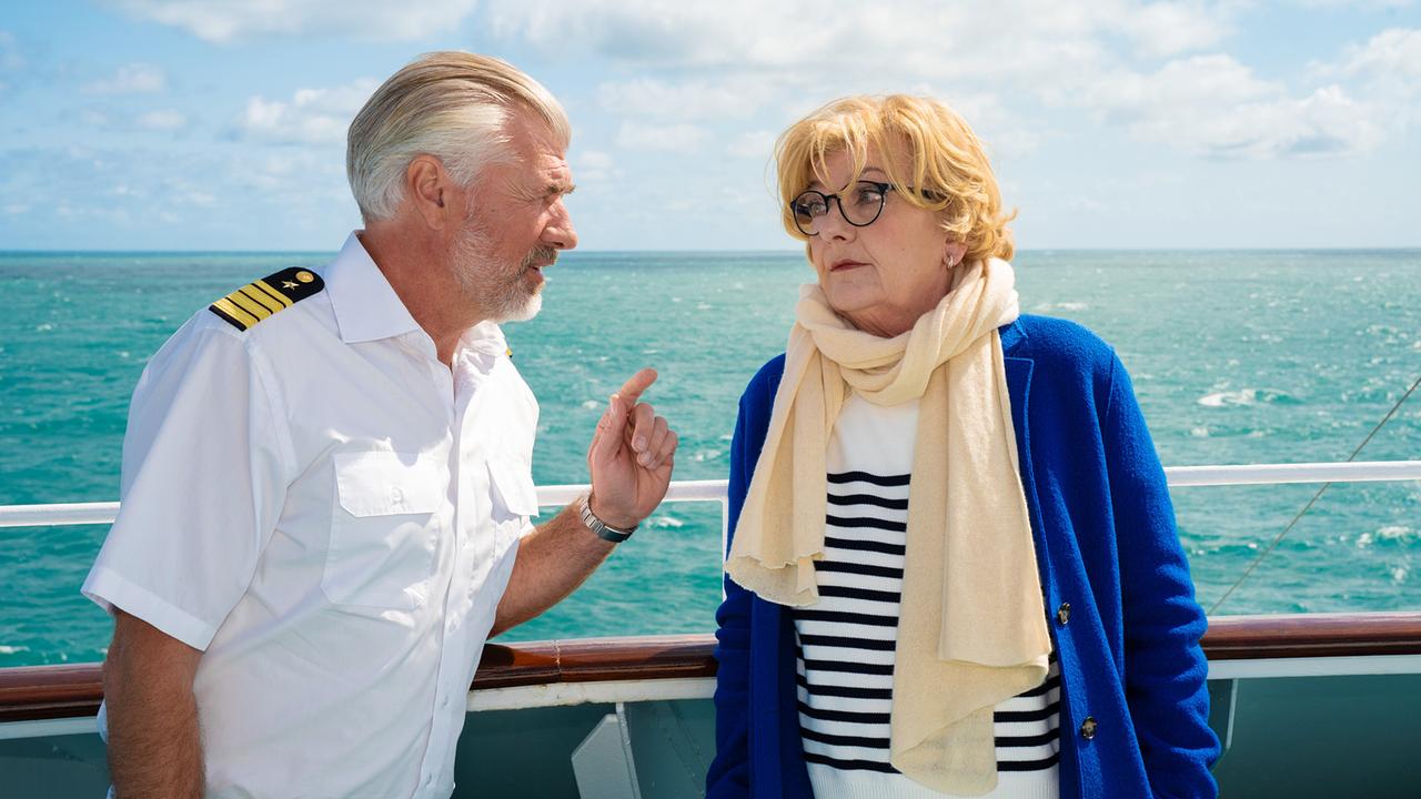 Staff-Kapitän Martin Grimm in Schiffsuniform spricht an der Reling eines Schiffes mit Evelyn Müller in Mantel und Schal vor offener Meereskulisse.