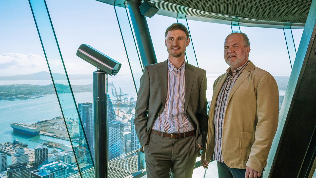 Marek Erhardt und Frédéric Brossier stehen auf einer verglasten Aussichtsplattform mit Blick auf eine Hafenstadt und das Meer im Hintergrund.