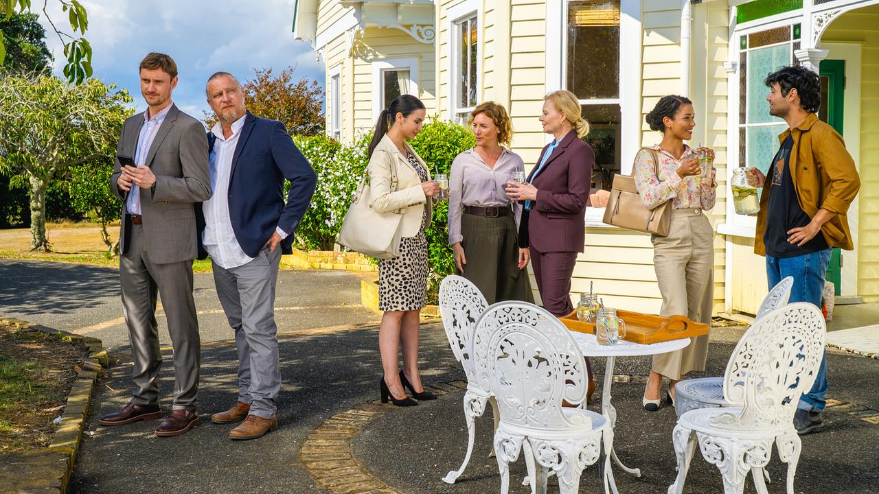 Susanna Simon mit ihrem Team stehen vor einem gelben Farmhaus und unterhalten sich bei Getränken im Freien.