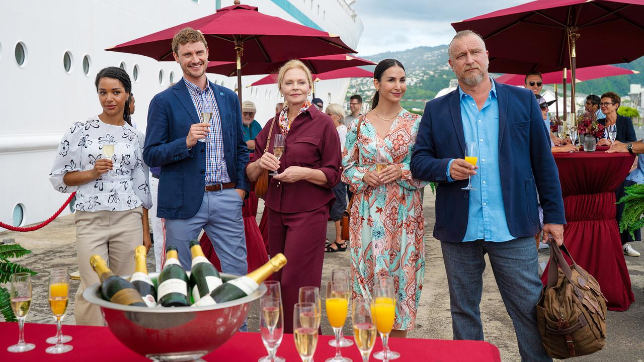 Sila Sahin, Luna Baptiste, Susanna Simon, Frédéric Brossier und Matthias Komm stehen mit Getränken vor dem Traumschiff bei einem Empfang mit Champagner. 