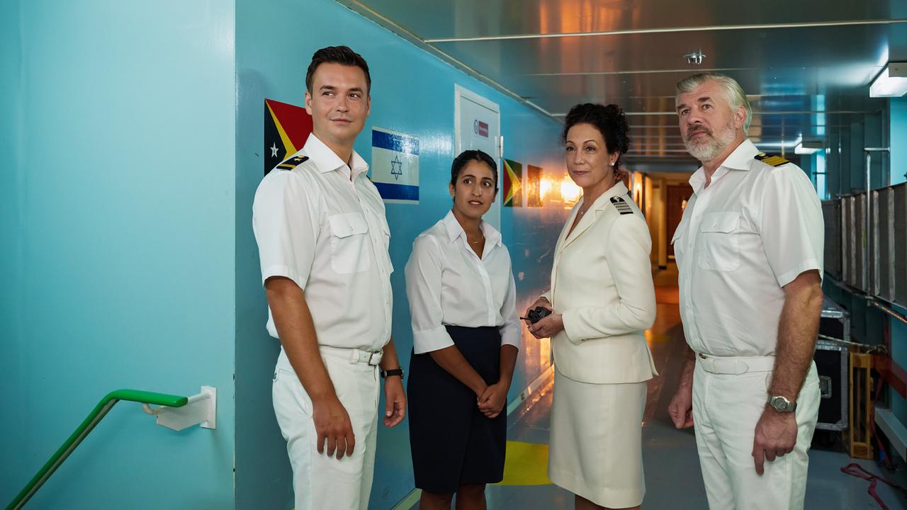 Die vier Crewmitglieder in Uniform, Hanna Liebhold, Staff-Kapitän Martin Grimm, Praktikantin Amrei Seibold und der nautische Offiziersassistent Noah Schütt, unterhalten sich im schmalen Gang eines Kreuzfahrtschiffs.