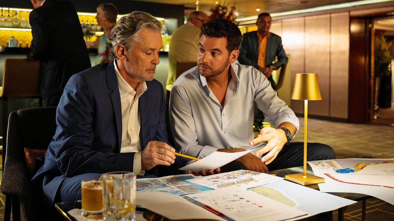 Basti Kugler und Ulrich von Stein begutachten Unterlagen und Karten in einer Schiffsbar.