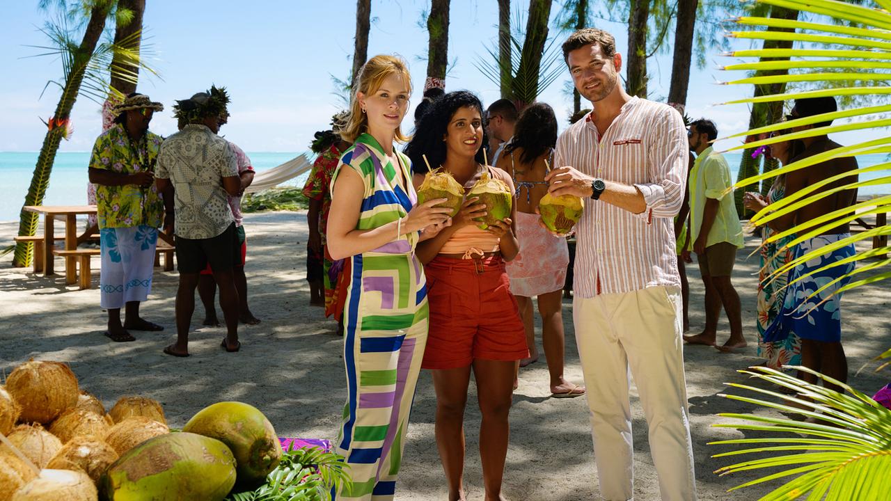 Toni Wittig, Amrei Seibold und Landschaftsgärtner Basti Kugler stehen beisammen und trinken frische Kokosnüsse bei einer Strandveranstaltung mit tropischer Kulisse.