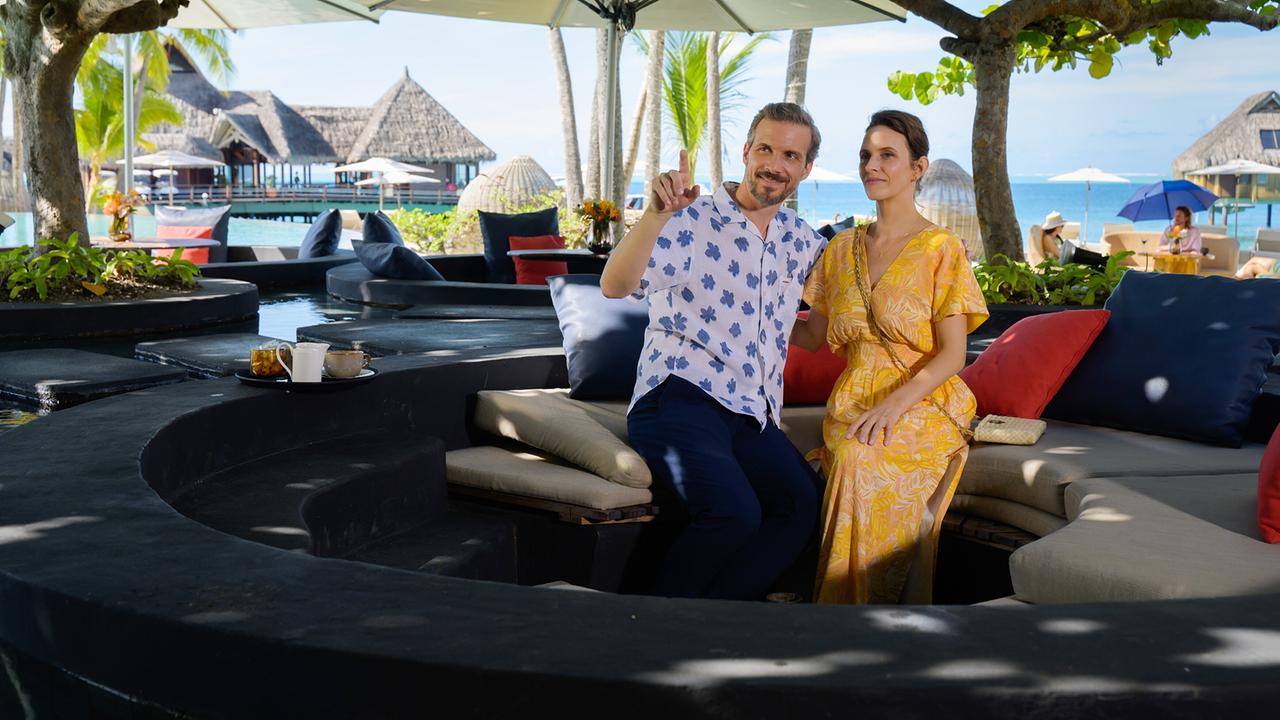 Paul Richter und Elsa Westrup sitzen entspannt in einer Lounge mit Blick auf das Meer und Überwasser-Bungalows.