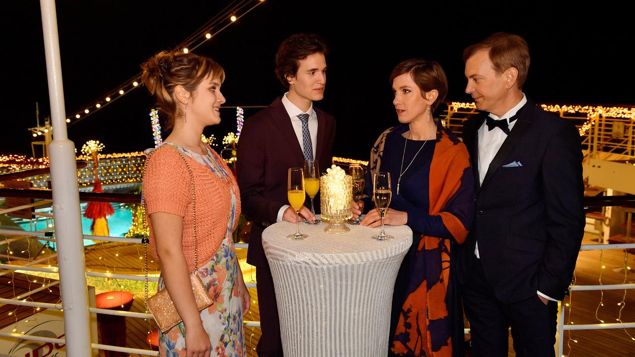 Lisa Sommer, Paul Wagner, Katja Sommer und Björn Wagner stehen festlich gekleidet bei Nacht an einem Stehtisch auf dem Deck eines Kreuzfahrtschiffs.