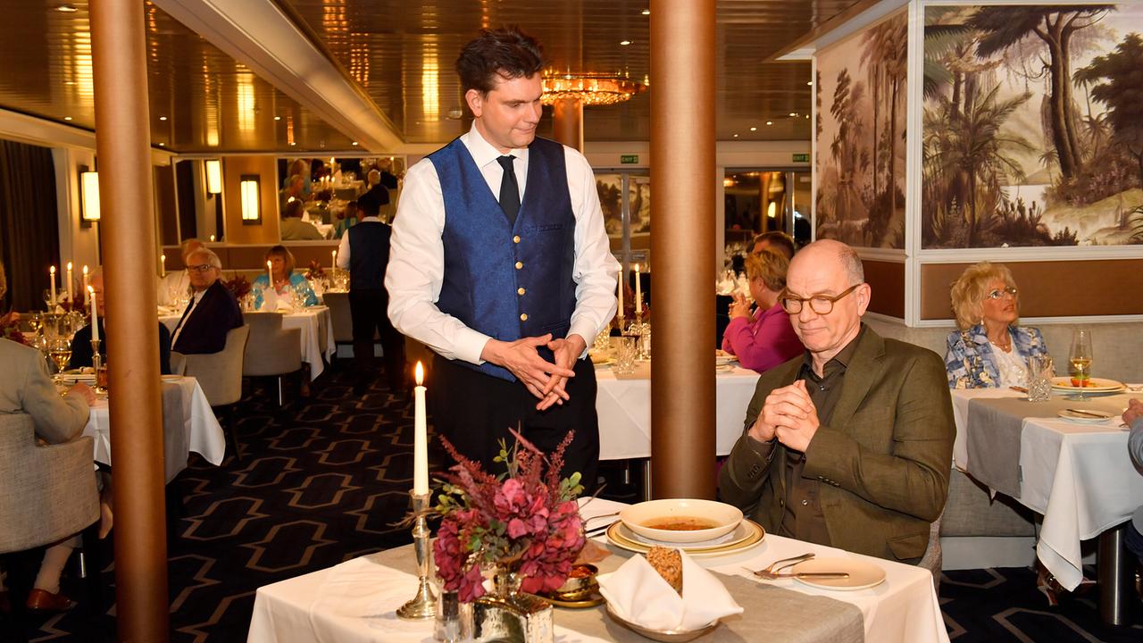 Kellner Peter bedient Gast Oliver Stiller im festlich gedeckten Speisesaal eines Schiffs.