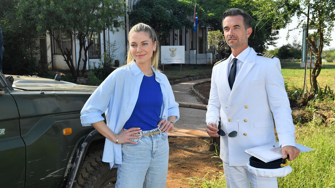 Kapitän Max Parger in weißer Uniform und Sophia Berg in Freizeitkleidung unterhalten sich vor einem Fahrzeug und dem  Krankenhaus in Madikwe.