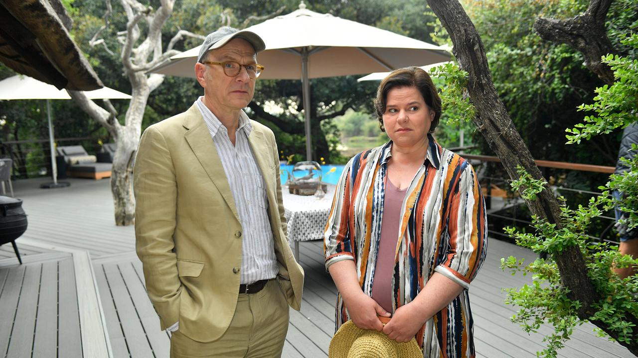 Oliver Stiller und Emilia Gronewald stehen auf einer Terrasse im Grünen, umgeben von Bäumen und Sonnenschirmen.