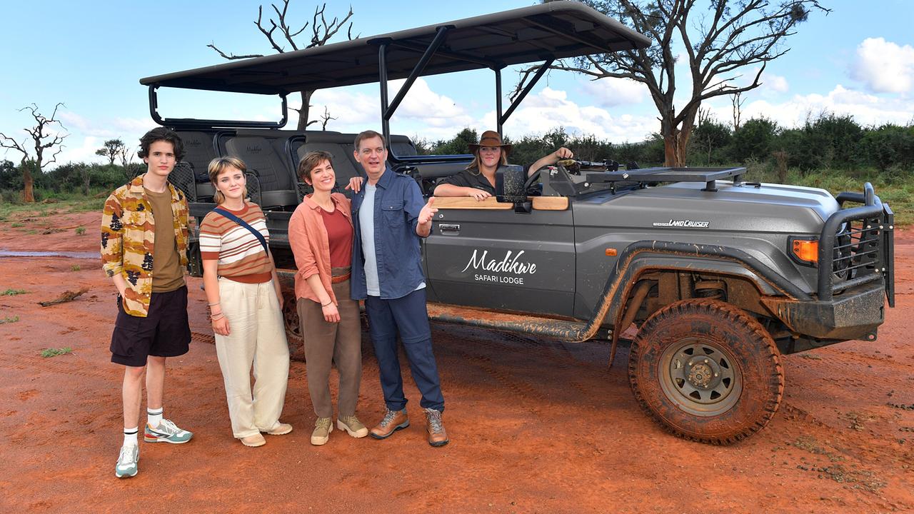 Katja und Lisa Sommer und Björn und Paul Wagner stehen bei einer Safari für ein Foto neben einem Geländewagen vor roter Erde und Buschlandschaft.