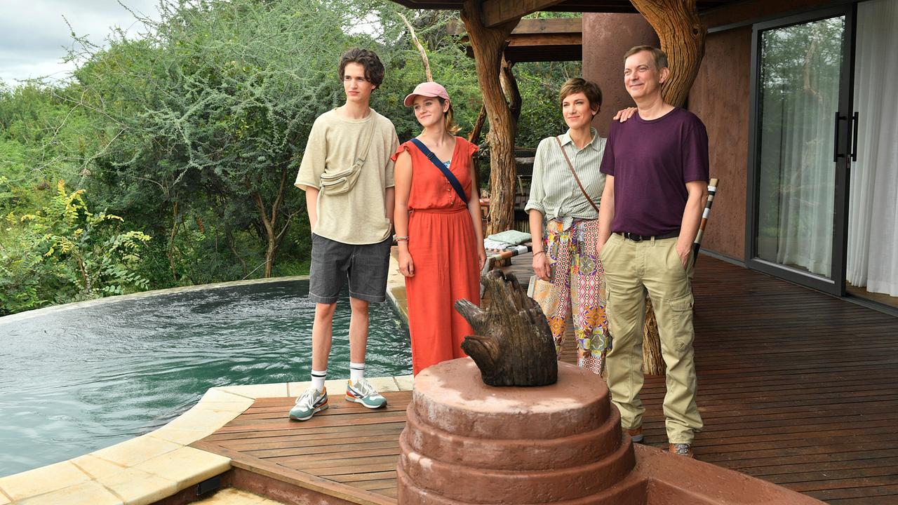 Katja Sommer und Björn Wagner stehen mit ihren Kindern Lisa Sommer und Paul Wagner am Rand eines Infinity‑Pools vor dichtem Grün und einer hölzernen Veranda.