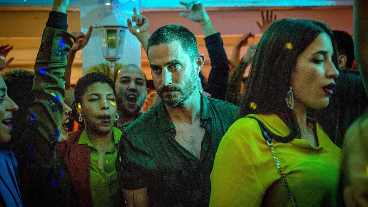 © ORF/Beta Film/Degeto/Victor Bello Kommissar Xavi Bonet steht in der Mitte tanzender Partygäste und fokussiert jemand