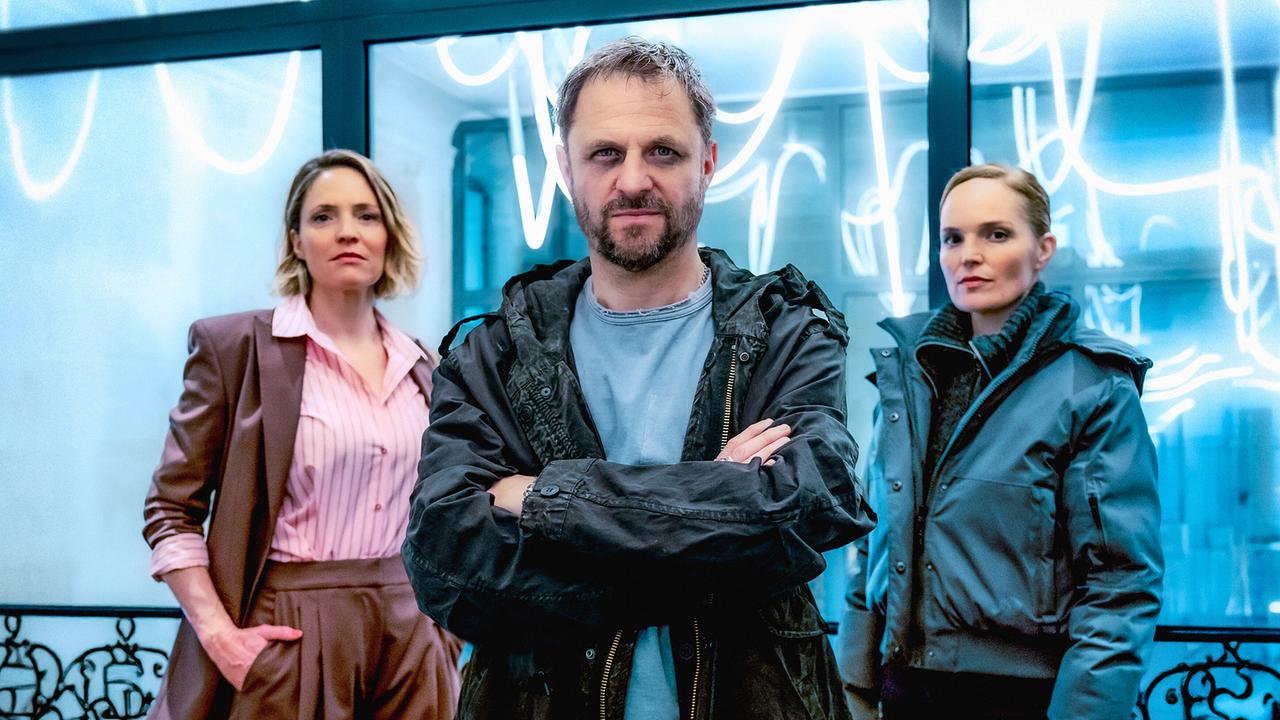 © ORF/Graf Film/Petro Domenigg Lukas Geier, Lara Schnee und Franziska Conte stehen vor einem neonröhrenbeleuchteten Raum zusammen und blicken in die Kamera.