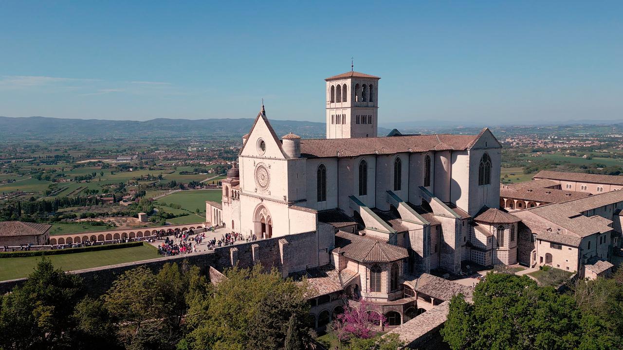 © ORF/Media Mediterranea/Lichtblick Film/Navigator Film/Paolo Colangeli Eine Luftaufnahme zeigt die Basilika des heiligen Franziskus vor der grünen Hügellandschaft im umbrischen Assisi, Italien