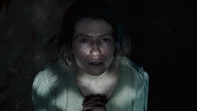 Agnes sitzt im Dunkeln mit gefalteten Händen, ein schmaler Lichtstrahl fällt auf ihr Gesicht.