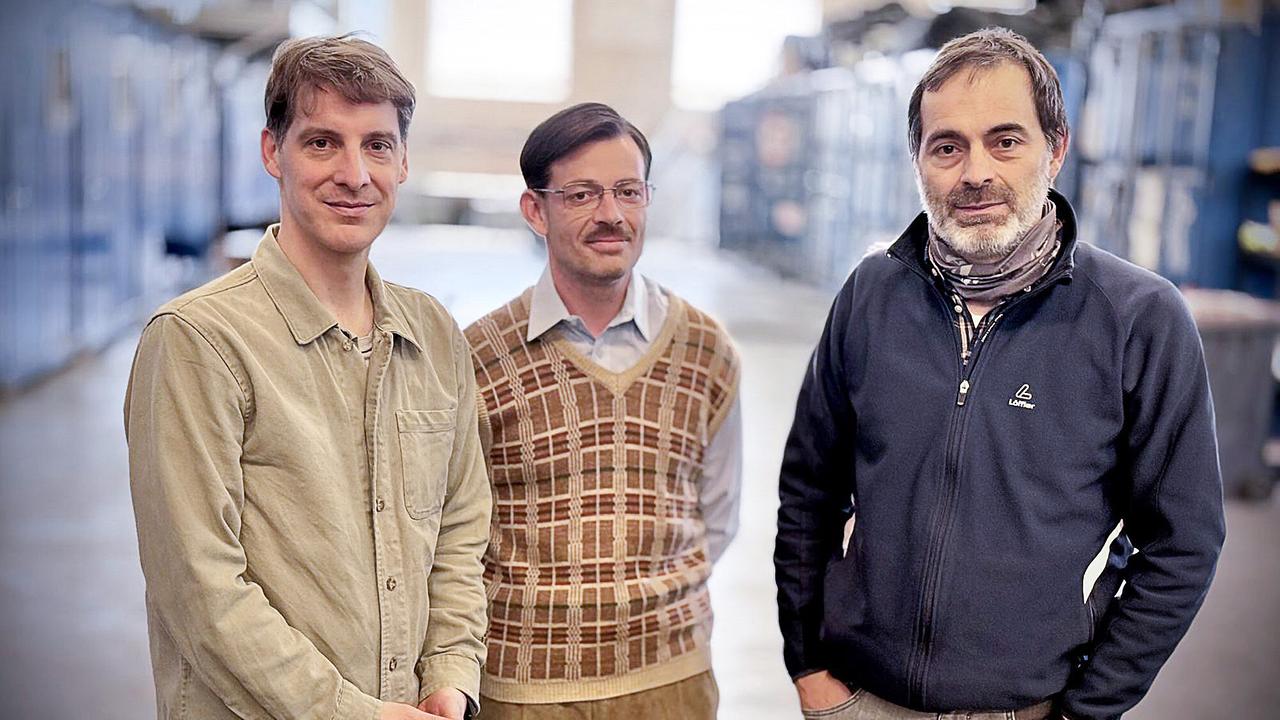 Fuchs-Darsteller Georg Elias Hengl steht mit Gregor Stuhlpfarrer und Georg Ransmayr, den Regisseuren der Dokumentation, in einer großen Lagerhalle. 