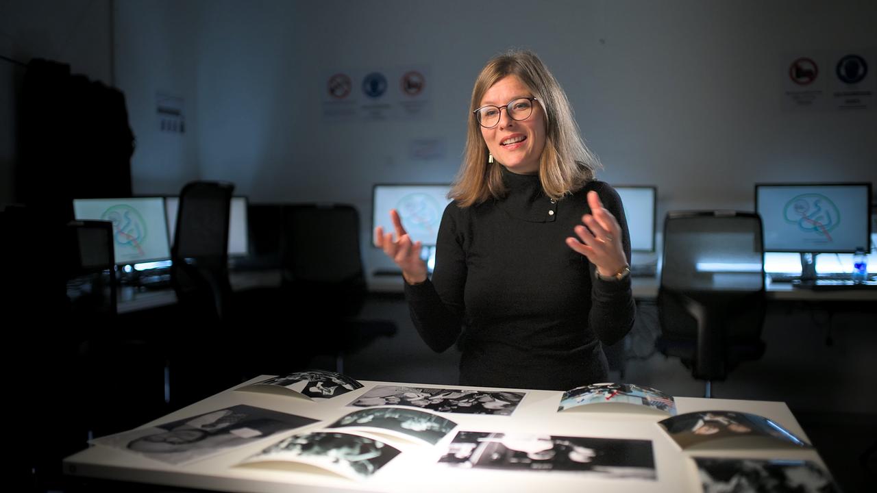 © ORF/ZDF/Jan Prillwitz Wissenschaftlerin erklärt, vor ihr Scharz-Weiß-Bilder, hinter ihr Computerbildschirm