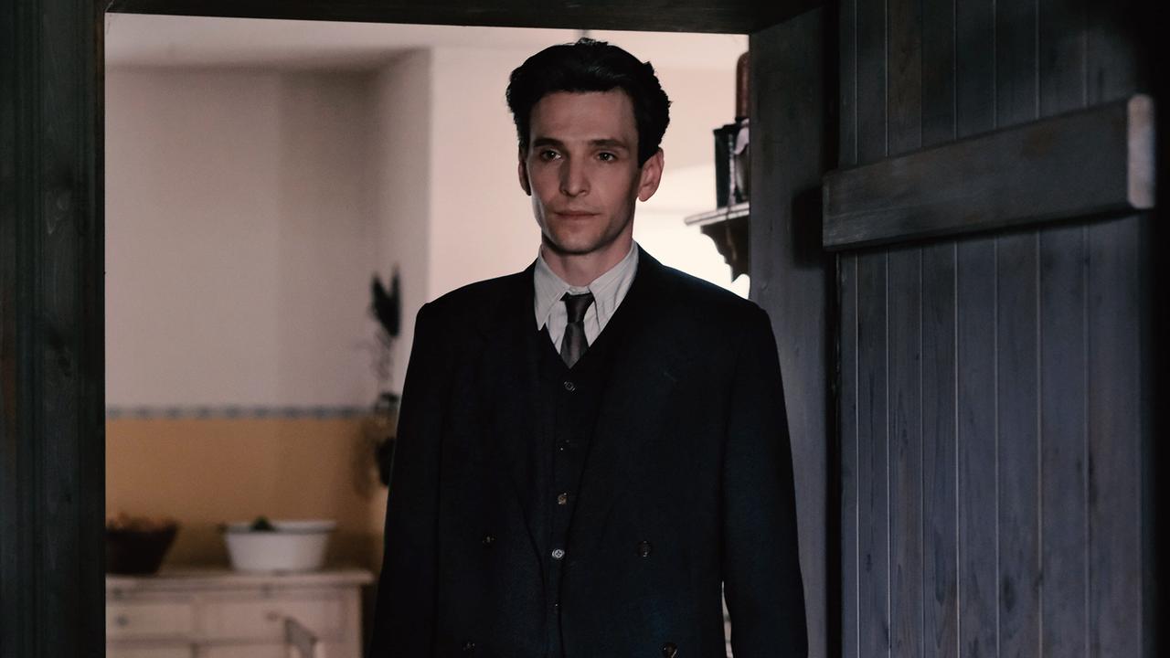 Franz Kafka steht in einer Türöffnung und blickt ernst in den Raum.