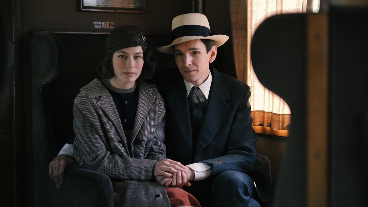 Dora und Franz Kafka sitzen eng beieinander in einem Zugabteil und halten sich an den Händen.