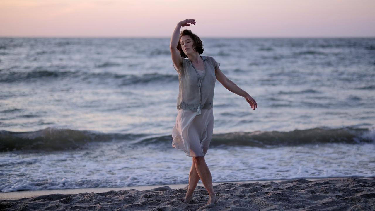 Dora tanzt barfuß am Strand bei sanftem Abendlicht.