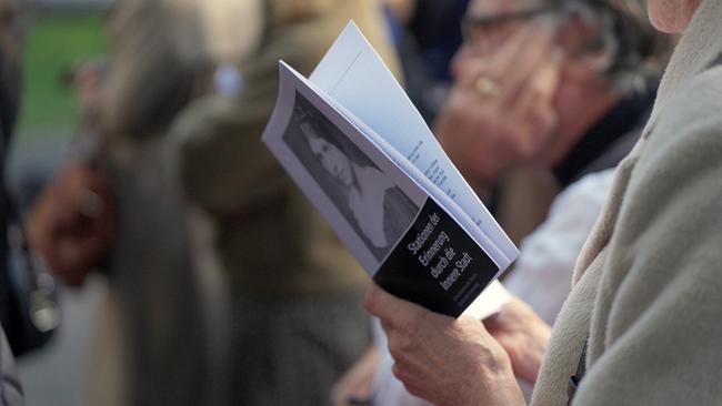 © ORF/Metafilm GmbH Bei der Veranstaltungseröffnung von "Steine der Erinnerung im 1. Bezirk" hält eine Person ein Heft mit dem Titel „Stationen der Erinnerung durch die Innere Stadt“ und einem Porträtfoto auf dem Cover.