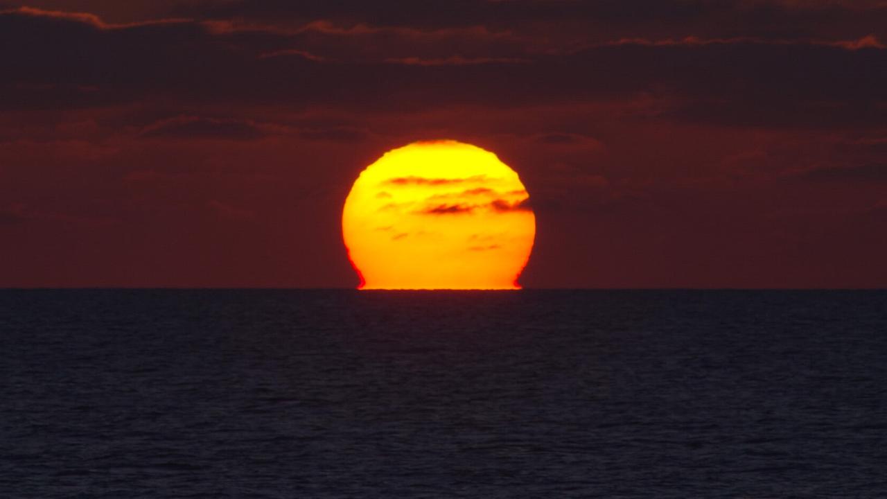 © ORF/Feature Filmproduktion/Fritz Kalteis Die leuchtend orange Sonne versinkt hinter dem Meer unter einem wolkenverhangenen Abendhimmel.