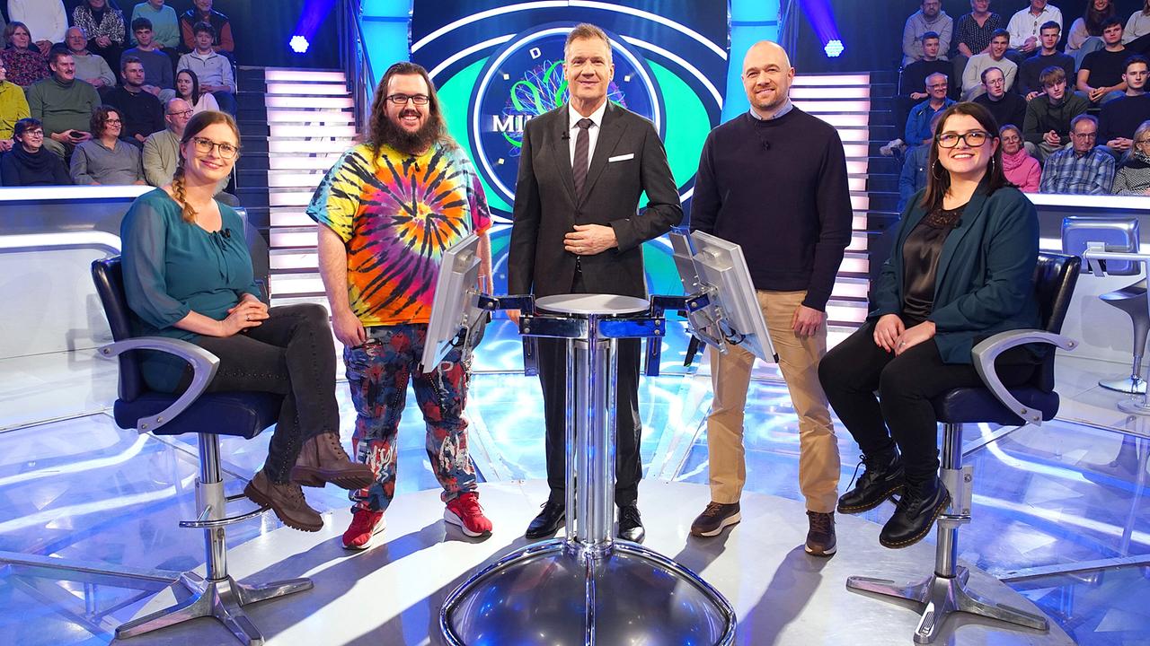 Ulrike Neumann, Stefan Reinisch, Armin Assinger, Christoph Friesinger und Madeleine Schwarz stehen um den Quizpult im "Millionenshow"-Studio, während das Publikum im Hintergrund zusieht.