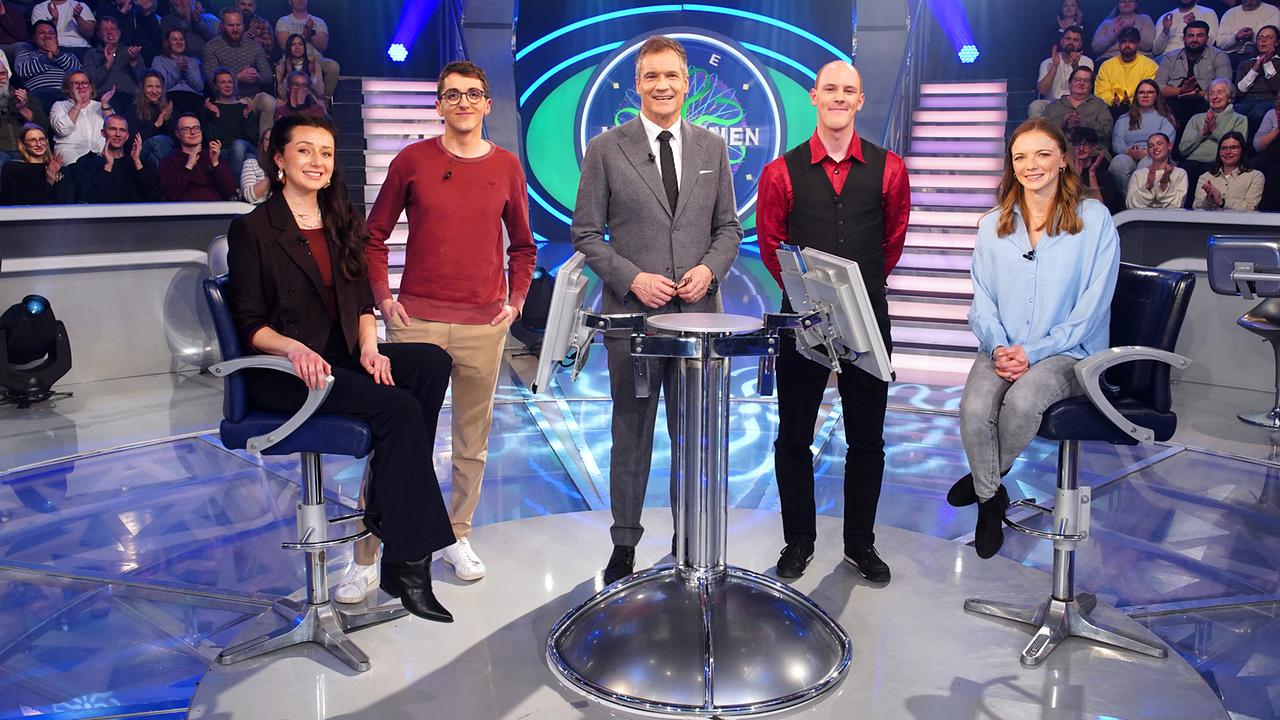 © ORF/Stefan Gregorowius Fee Louise Schwarz, Dominik Primus, Armin Assinger, Jan Leopold und Astrid Mathy stehen gemeinsam um den "Millionenshow"-Pult im TV-Studio mit Publikum im Hintergrund.