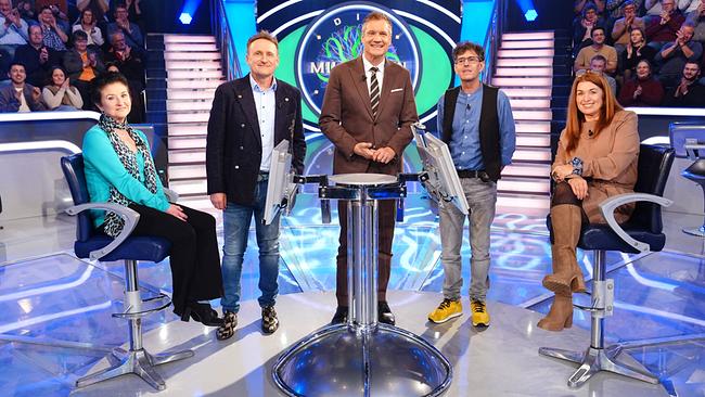 Im hell beleuchteten "Millionenshow"-Studio stehen und sitzen Marina Achitz, Ferenc Ullmann, Wolfgang Peer und Manuela Voithofer mit Armin Assinger in der Mitte um den Quiz-Pult, während ein applaudierendes Publikum im Hintergrund zu sehen ist.