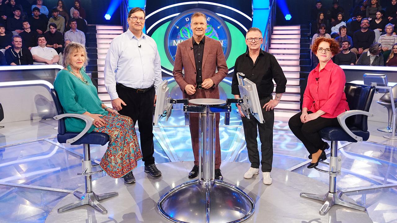 Edith Grünbichler, Martin Koch, Armin Assinger, Christian Feichter und Gabriele Dumps stehen gemeinsam um den "Millionenshow"-Pult im TV-Studio mit Publikum im Hintergrund.