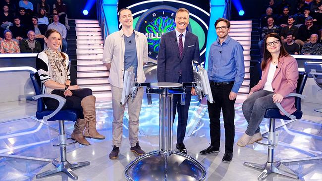 Tao Spielmann, Peter Litzlbauer, Armin Assinger, Manuel Nussbaumer und Sabine Lasinger stehen gemeinsam um den "Millionenshow"-Pult im TV-Studio mit Publikum im Hintergrund.