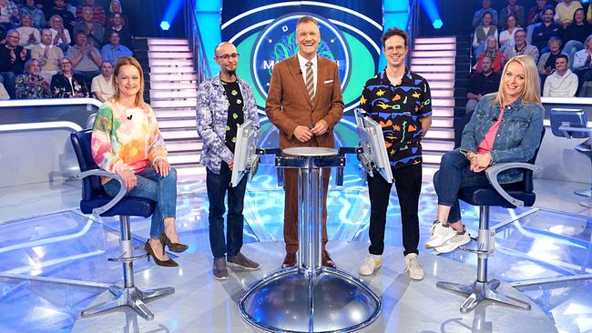 Renate Schrempf, David Ried, Armin Assinger, Stefan Ebner-Benke und Michaela Heese stehen gemeinsam um den "Millionenshow"-Pult im TV-Studio mit Publikum im Hintergrund.