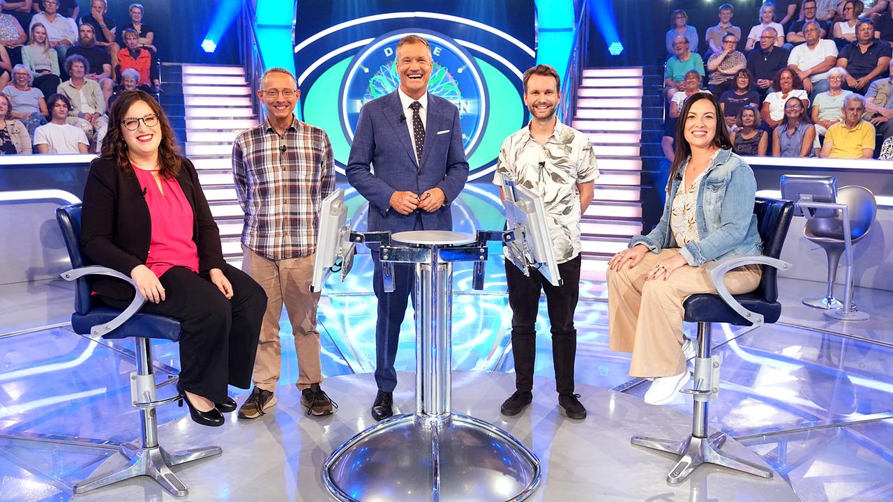 © ORF/Stefan Gregorowius Lucia Huemer, Armin Schmidhofer, Armin Assinger, Andreas Prentner und Petra Schmolz stehen lächelnd um den "Millionenshow"-Pult im TV-Studio mit Publikum im Hintergrund.