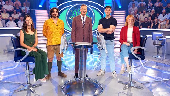 © ORF/Stefan Gregorowius Julia Avi, Manuel Rom, Armin Assinger, Philipp Bogner und Nina Schwaiger stehen lächelnd um den "Millionenshow"-Pult im TV-Studio mit Publikum im Hintergrund.